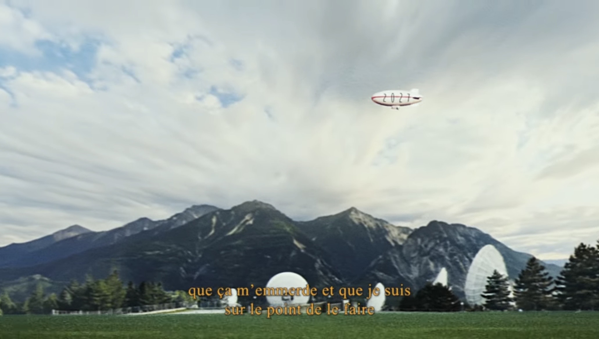 A mountain landscape under a wide sky, a small airship floating above
